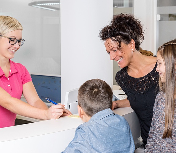 Mother and children filling out dental insurance forms at dental office reception desk