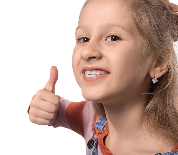 Young child giving thumbs up for orthodontic treatment