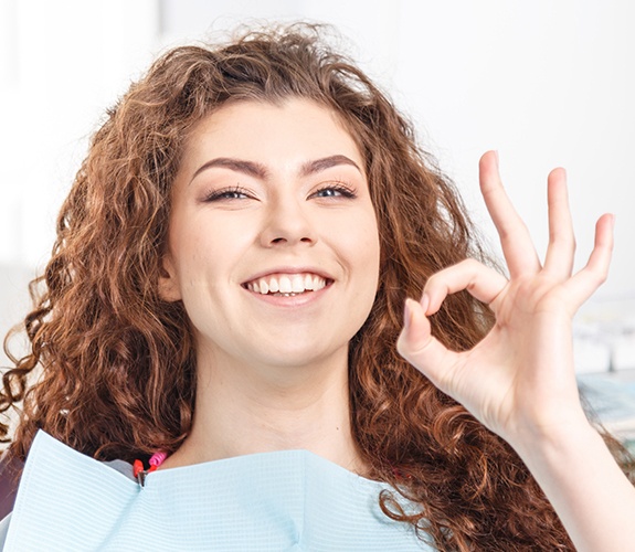 Woman giving okay sign after professional dental cleaning
