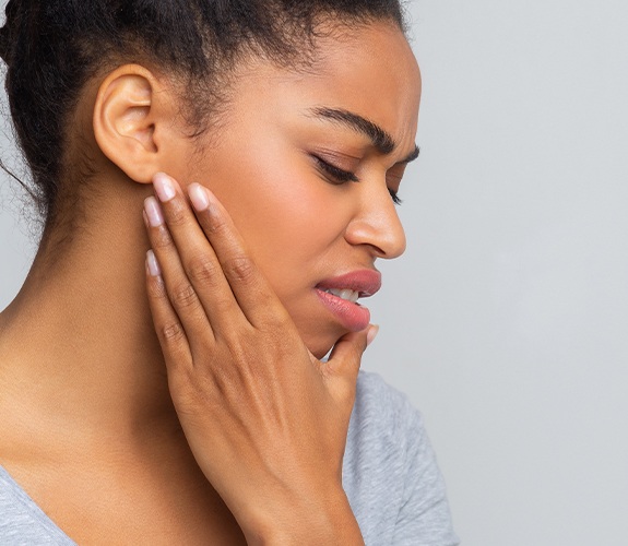 Woman in need of T M J treatment holding jaw in pain