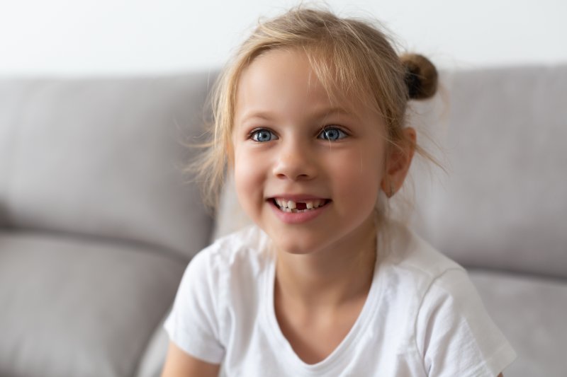 Little girl with missing tooth laughing on couch