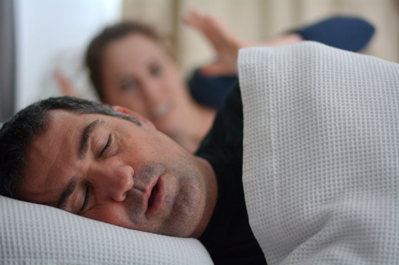middle-aged man snoring while wife appears frustrated