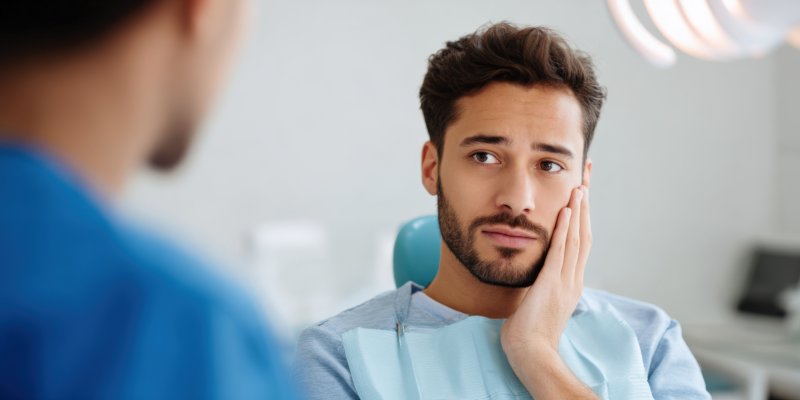 male patient holding cheek and talking to dentist